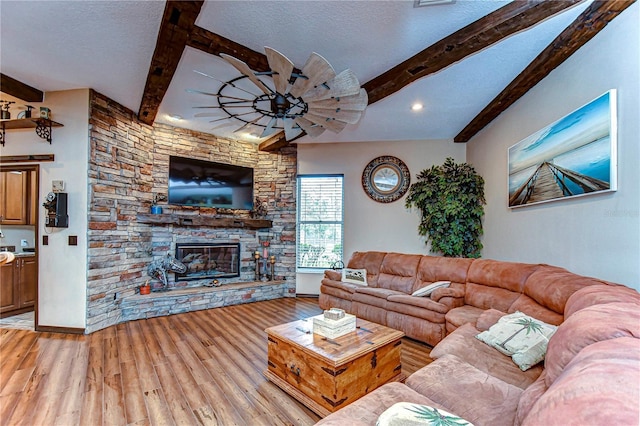 living room featuring beam ceiling, a stone fireplace, light hardwood / wood-style flooring, and a textured ceiling