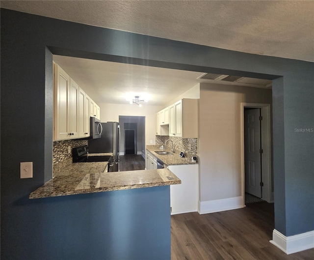 kitchen featuring stainless steel appliances, a peninsula, stone countertops, and white cabinets