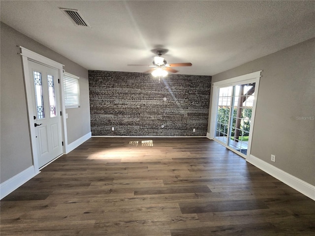 interior space with a textured ceiling, an accent wall, dark wood-style flooring, visible vents, and baseboards