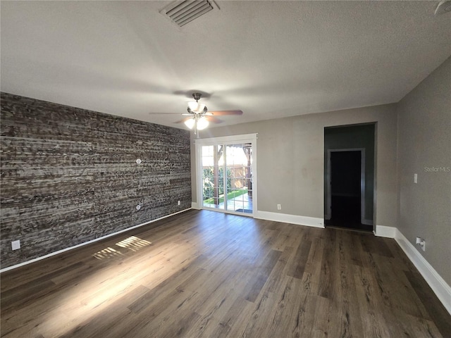 empty room with visible vents, baseboards, dark wood finished floors, a ceiling fan, and an accent wall