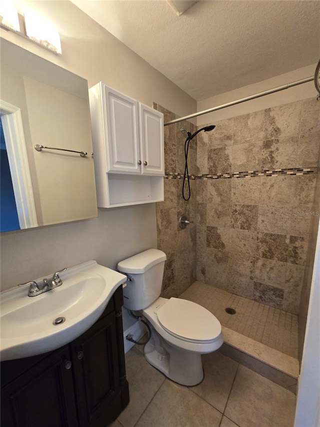 full bathroom featuring toilet, tile patterned flooring, a tile shower, a textured ceiling, and vanity