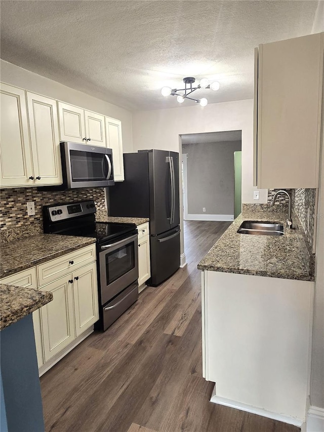 kitchen with stainless steel appliances, decorative backsplash, dark wood-type flooring, a sink, and dark stone countertops