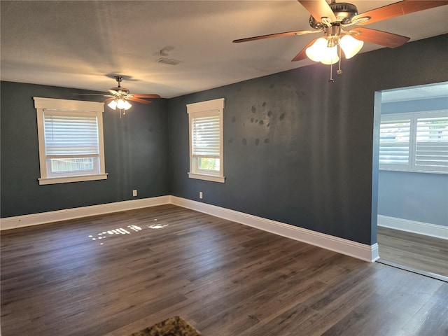 empty room with a healthy amount of sunlight, dark wood-style floors, ceiling fan, and baseboards