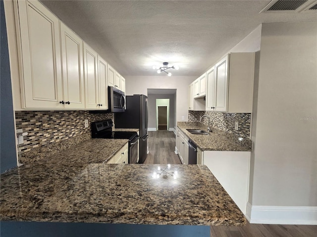 kitchen featuring visible vents, appliances with stainless steel finishes, a sink, dark stone counters, and a peninsula