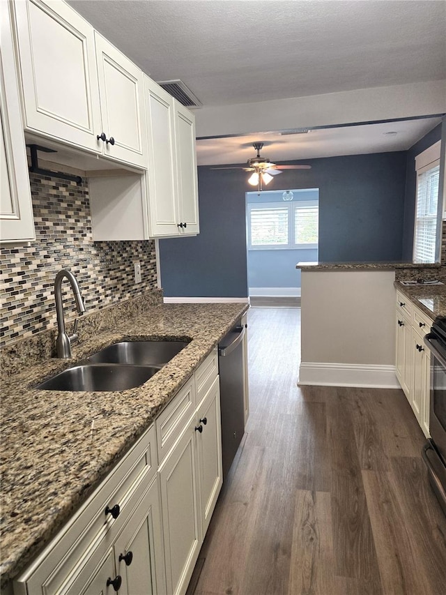 kitchen with stainless steel dishwasher, dark wood-type flooring, white cabinetry, a sink, and dark stone countertops