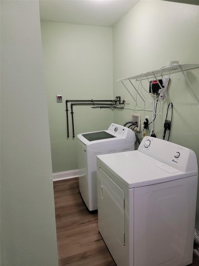 washroom featuring laundry area, separate washer and dryer, wood finished floors, and baseboards