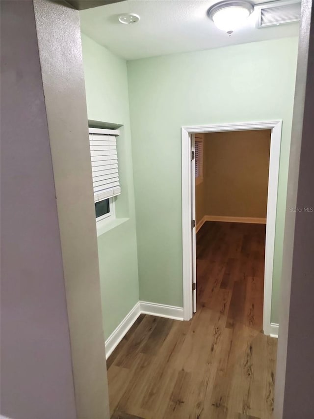 hallway featuring visible vents, baseboards, and wood finished floors