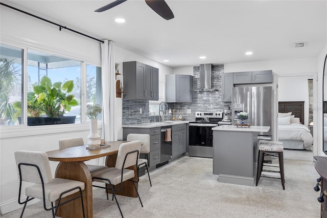 kitchen with a center island, wall chimney range hood, gray cabinets, a breakfast bar, and appliances with stainless steel finishes