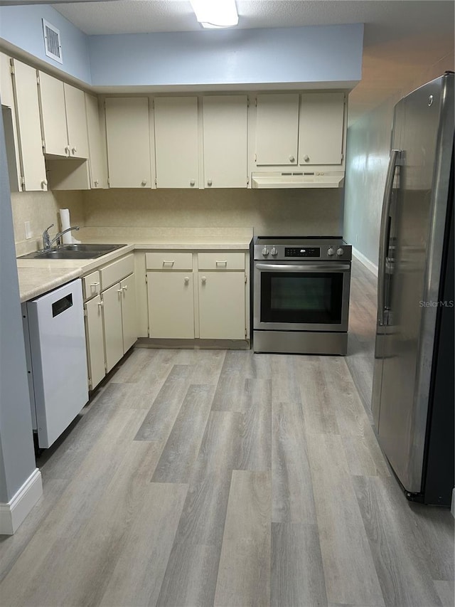 kitchen with light hardwood / wood-style floors, sink, appliances with stainless steel finishes, and cream cabinetry