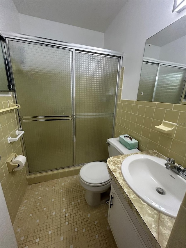 bathroom with toilet, vanity, tile walls, tile patterned floors, and a shower with door