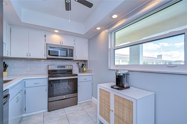 kitchen with ceiling fan, a raised ceiling, backsplash, white cabinets, and appliances with stainless steel finishes