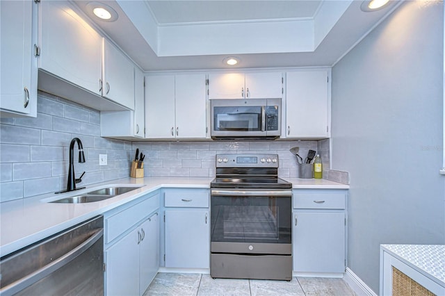 kitchen featuring backsplash, stainless steel appliances, a tray ceiling, sink, and white cabinets