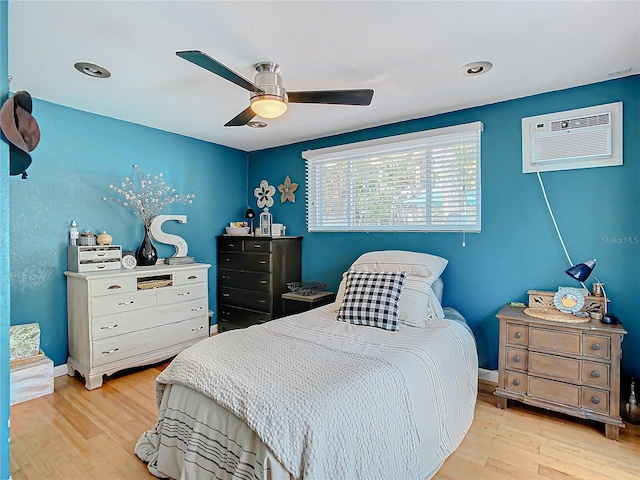 bedroom featuring light hardwood / wood-style flooring, ceiling fan, and a wall unit AC