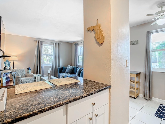 kitchen featuring ceiling fan, dark stone countertops, white cabinetry, and light tile patterned floors