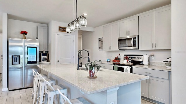 kitchen with light stone counters, decorative light fixtures, a kitchen bar, a kitchen island with sink, and appliances with stainless steel finishes