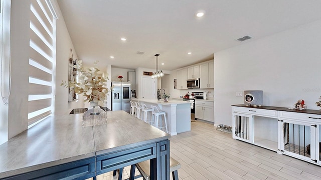 kitchen with appliances with stainless steel finishes, a breakfast bar, a center island with sink, white cabinetry, and hanging light fixtures