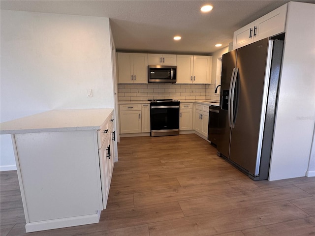 kitchen with light wood-type flooring, tasteful backsplash, stainless steel appliances, sink, and white cabinets