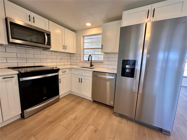 kitchen featuring stainless steel appliances, white cabinetry, light hardwood / wood-style floors, and sink