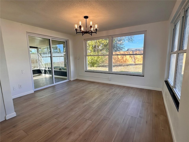 unfurnished dining area featuring wood-type flooring, a textured ceiling, and a chandelier