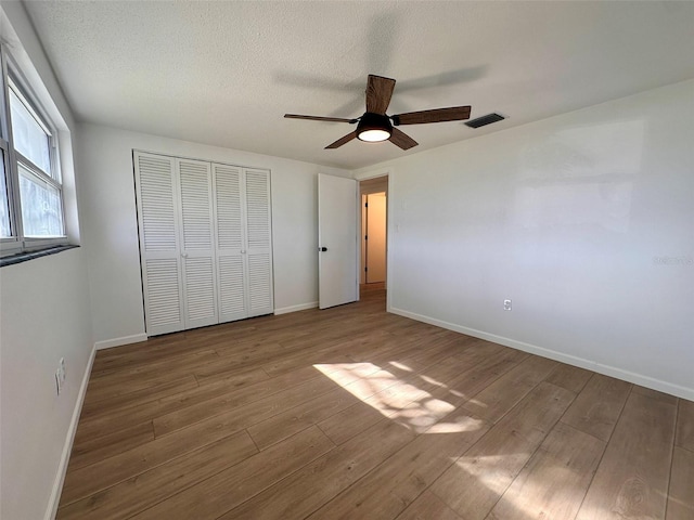 unfurnished bedroom with a closet, a textured ceiling, hardwood / wood-style flooring, and ceiling fan