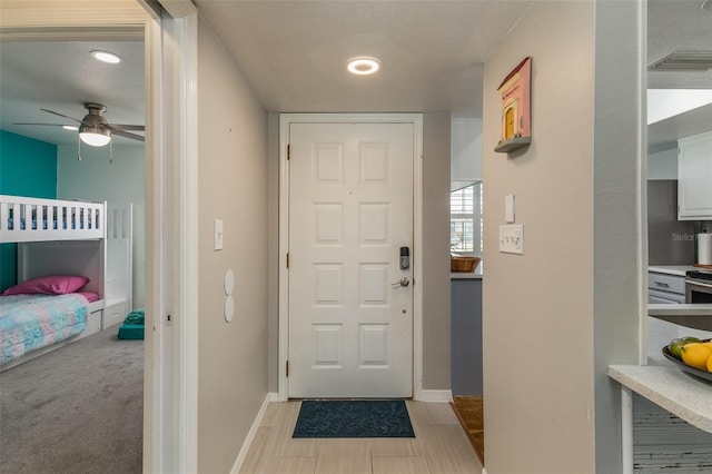 entrance foyer with ceiling fan, light colored carpet, and a textured ceiling