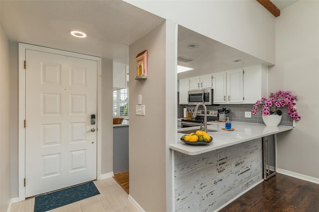 kitchen with white cabinetry, kitchen peninsula, decorative backsplash, appliances with stainless steel finishes, and hardwood / wood-style flooring