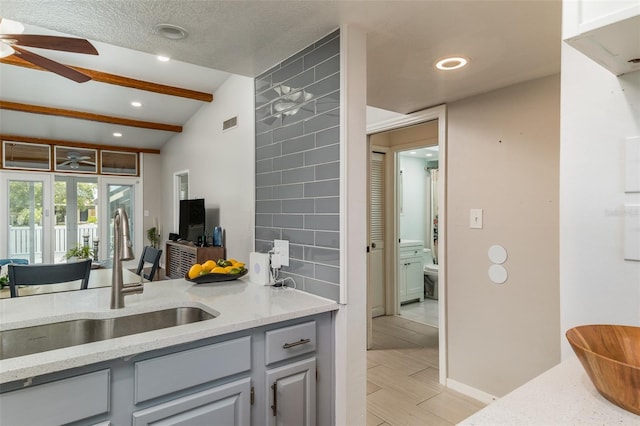 kitchen featuring light stone countertops, sink, ceiling fan, vaulted ceiling with beams, and gray cabinets