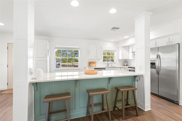 kitchen with light wood-type flooring, white cabinetry, a kitchen bar, kitchen peninsula, and stainless steel appliances