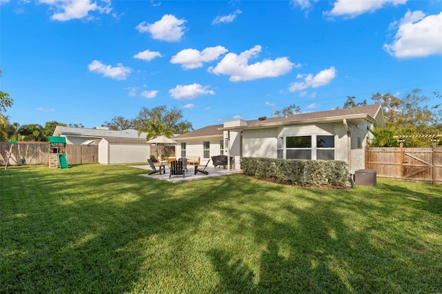 rear view of property with a playground, a patio area, a lawn, and a storage unit