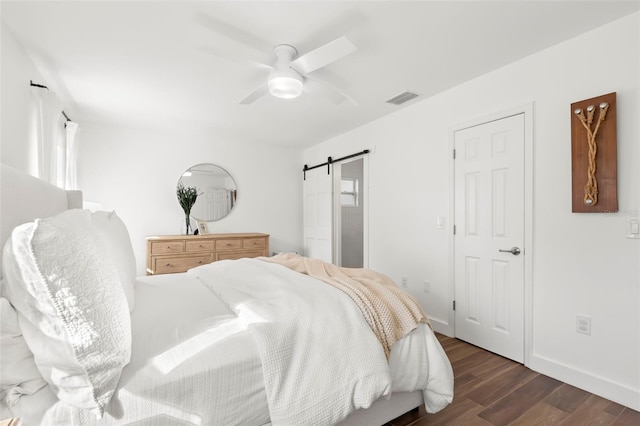 bedroom with ceiling fan, a barn door, and dark hardwood / wood-style flooring