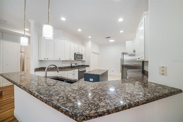 kitchen featuring kitchen peninsula, stainless steel appliances, sink, a center island, and hanging light fixtures