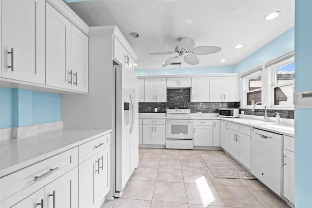 kitchen with light stone counters, white appliances, ceiling fan, sink, and white cabinetry