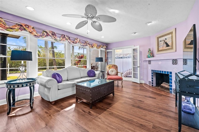 living room featuring hardwood / wood-style flooring, ceiling fan, a textured ceiling, and a tile fireplace