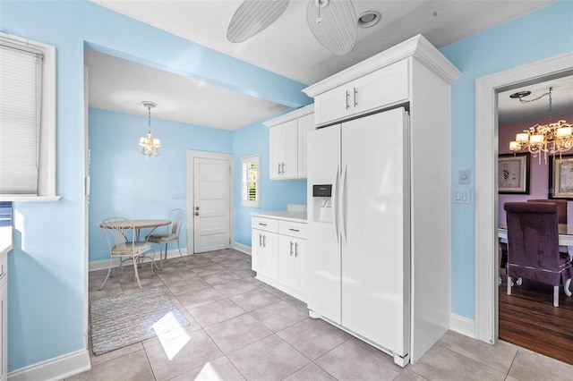 kitchen featuring ceiling fan with notable chandelier, white refrigerator with ice dispenser, light tile patterned floors, decorative light fixtures, and white cabinetry