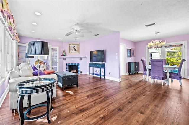 living room featuring ceiling fan with notable chandelier, dark hardwood / wood-style flooring, a textured ceiling, and a tile fireplace