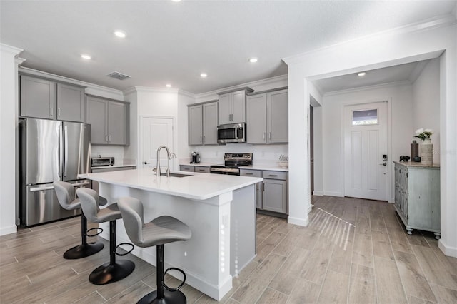 kitchen with gray cabinetry, sink, stainless steel appliances, an island with sink, and a breakfast bar area