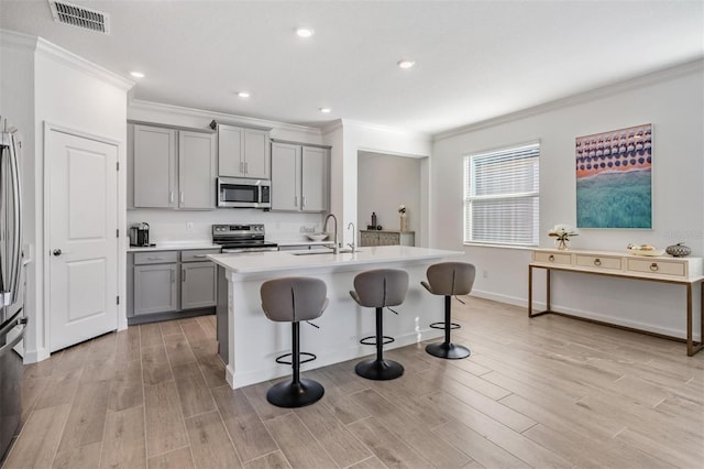 kitchen featuring appliances with stainless steel finishes, gray cabinets, and a center island with sink