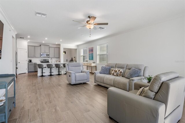 living room with ceiling fan, sink, light wood-type flooring, and crown molding