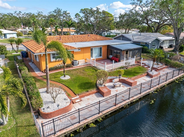 rear view of property featuring a lawn, a sunroom, central air condition unit, a water view, and a patio