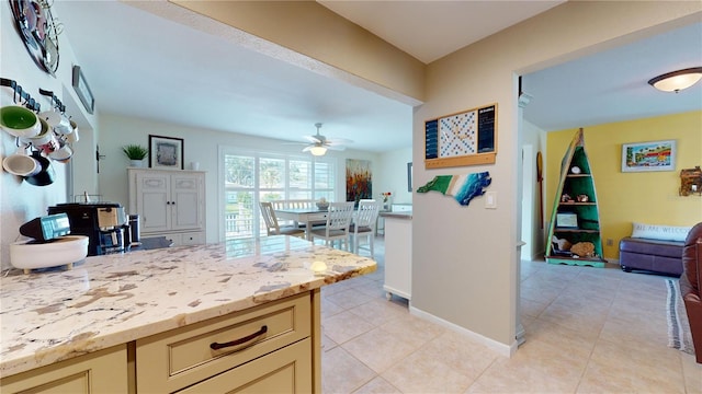 kitchen with ceiling fan, cream cabinets, light tile patterned floors, and light stone countertops