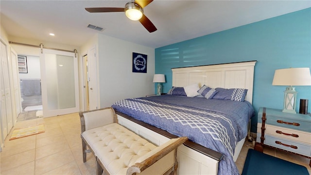 bedroom featuring a barn door, ensuite bath, ceiling fan, and light tile patterned flooring