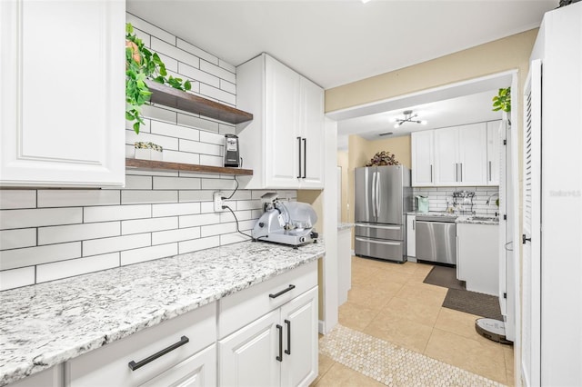 kitchen featuring tasteful backsplash, light stone counters, stainless steel appliances, white cabinetry, and light tile patterned flooring