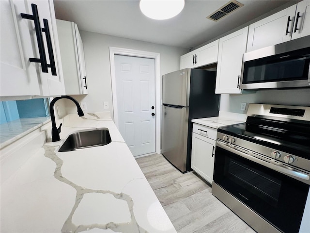 kitchen with white cabinets, sink, light hardwood / wood-style floors, light stone counters, and stainless steel appliances