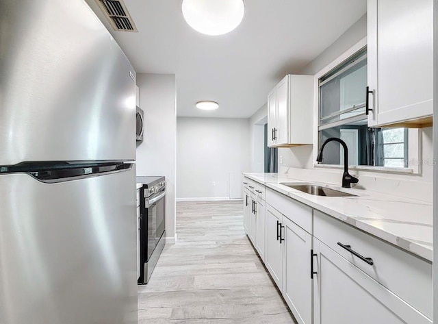 kitchen with sink, white cabinetry, stainless steel appliances, light stone counters, and light wood-type flooring