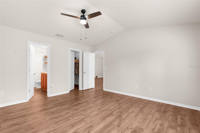 unfurnished bedroom with light wood-type flooring, a walk in closet, ensuite bath, ceiling fan, and a closet