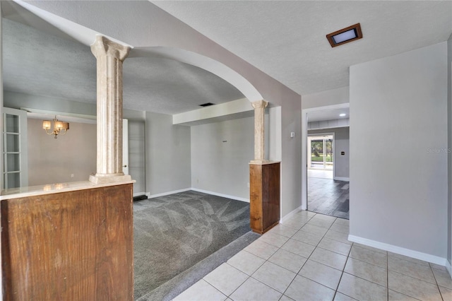 empty room with a textured ceiling, decorative columns, light colored carpet, and a notable chandelier