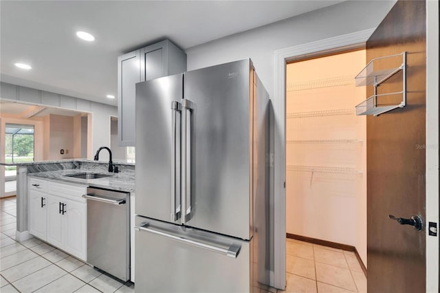 kitchen with light stone countertops, sink, light tile patterned floors, white cabinets, and appliances with stainless steel finishes