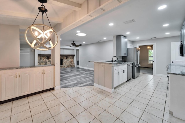 kitchen with stainless steel appliances, light stone counters, pendant lighting, a fireplace, and ceiling fan with notable chandelier