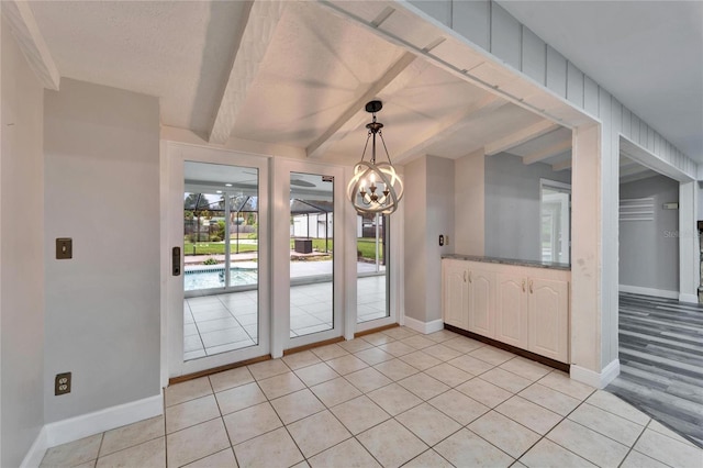 unfurnished dining area featuring a notable chandelier, beam ceiling, light tile patterned floors, and a textured ceiling