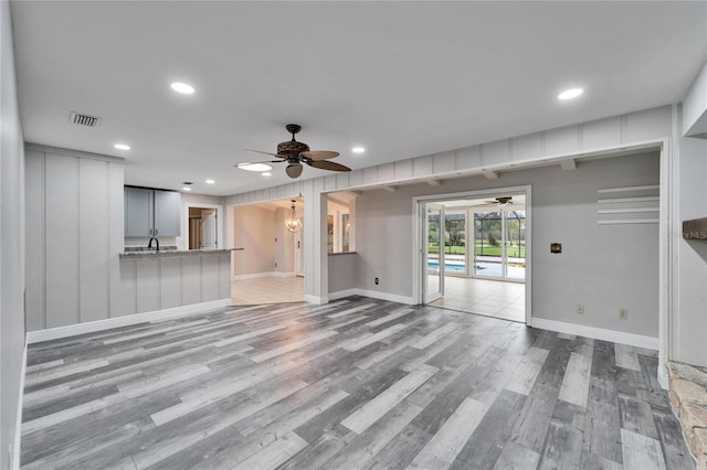 unfurnished living room featuring sink, light hardwood / wood-style floors, and ceiling fan with notable chandelier